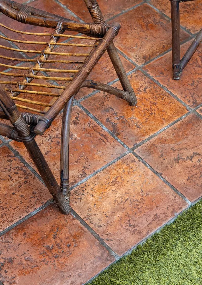 Terrasse mit Cottoboden mit dunkler Patina und Rattanstuhl